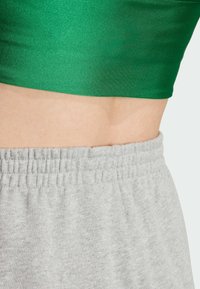 Žalias trumpas viršus iš blizgaus audinio, derinamas su pilkomis sportinėmis kelnėmis, turinčiomis elastingą juosmenį ir minkštą, tekstūruotą medžiagą.