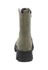 Bota de ante verde hasta el tobillo con una suela de goma negra resistente, que presenta un zipper lateral y una textura suave. La parte trasera muestra un detalle del logo cerca de la base.