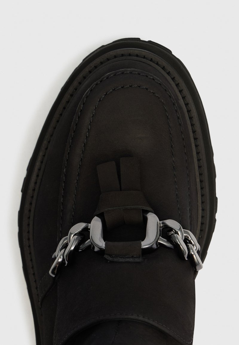 Schwarzer Lederloafer mit abgerundeter Spitze und silberner Ketten- und Schnallenverzierung oben, vor einem schlichten weißen Hintergrund.