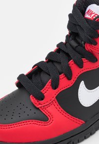 Nike högkvalitativ sneakers med svart läder, röda accenter och en vit swoosh. Texturerade svarta skosnören och perforerad tådetalj är synliga.