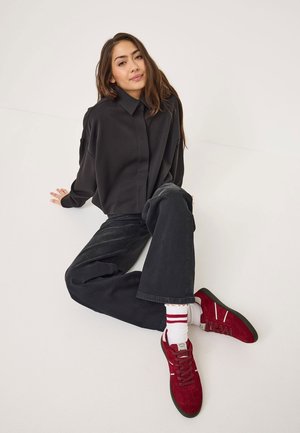 Black long-sleeve shirt, relaxed black pants, red suede sneakers with white accents, and ribbed white socks with red stripes.