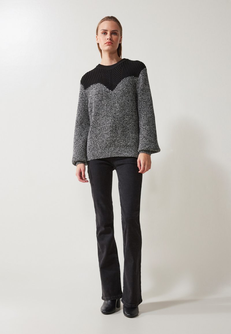 Sweter dzianinowy w kolorze czarnym i szarym, z teksturowanym, prążkowanym dekoltem oraz obszernymi rękawami. Połączony z czarnymi spodniami w kant i czarnymi botkami.