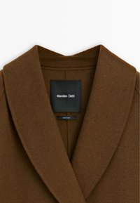 Brązowy wełniany płaszcz z szerokim kołnierzem, prostymi liniami i czarną metką z napisem "Massimo Dutti". Gładka tekstura i zorganizowany fason.