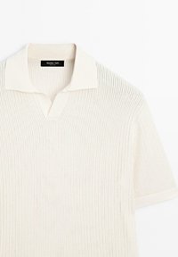 Polo en maille écru à manches courtes, avec une texture côtelée et un petit col, posé à plat sur un fond blanc.