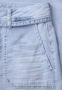 Zbliżenie na jasnoniebieskie dżinsy z denimu, pokazujące pas z pętlą na pasek i przednią kieszeń z widocznymi detalami szwów.