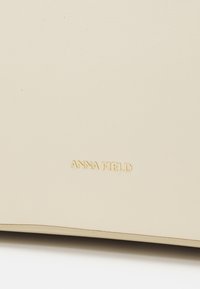 Surface en cuir couleur crème avec un petit texte doré embossé "ANNA FIELD" près du bord inférieur.