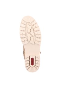 Semelle de chaussure beige avec des crampons profonds, présentant un logo rouge. La semelle en caoutchouc est texturée pour une meilleure adhérence et conçue pour la durabilité.