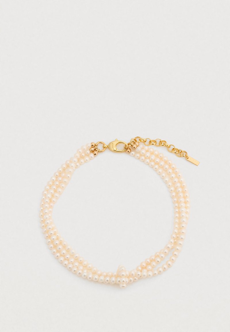 Trois rangs de petites perles blanc cassé avec un fermoir mousqueton en or et une chaîne d'extension, présentant une finition texturée et une forme arrondie.