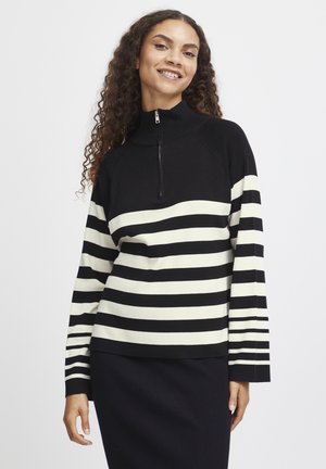 Pull-over rayé noir et blanc avec un col zippé mi-hauteur, présentant un tricot texturé. Manches longues avec un motif rayé s'étendant jusqu'aux poignets.