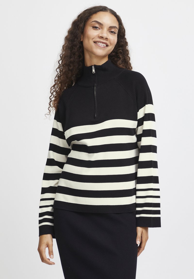 Pull-over rayé noir et blanc avec un col zippé mi-hauteur, présentant un tricot texturé. Manches longues avec un motif rayé s'étendant jusqu'aux poignets.