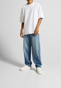 Camiseta blanca de gran tamaño, vaqueros holgados de color azul claro y zapatillas blancas. La camiseta tiene un cuello redondo; los vaqueros tienen un lavado desgastado.