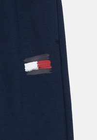 Námornícke modré tepláky s natretým pruhovaným vzorom v bielej, červenej a sivej farbe na ľavej strane. Vyrobené z textúrovaného bavlneného materiálu.