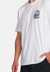 White cotton t-shirt with short sleeves, featuring a colorful graphic of a sunset and palm trees on the left chest. Relaxed fit.
