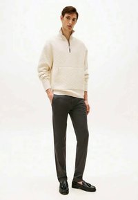 Light cream pullover with a textured diamond pattern, half-zip collar; paired with dark gray trousers and black loafers. Minimalist design.