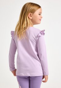 Πουκάμισο με μακριά μανίκια σε λιλά χρώμα, με διακοσμητικές βολάν στους ώμους, φτιαγμένο από απαλό ύφασμα. Συνδυάζεται με παντελόνι σε ίδιο λιλά χρώμα με floral σχέδιο.