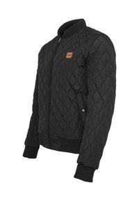 Čierna prešívaná bomber bunda s ribbovaným golierom a manžetami, s malou hnedou koženou nášivkou na hrudníku a s patentkami na stranách.