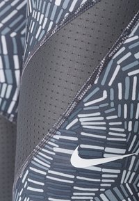 Nike sportovní legíny s šedým vzorem a bílými akcenty, vyrobené z prodyšného materiálu s perforacemi a plochými švy.