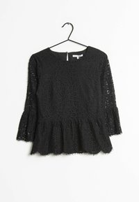 Top in pizzo nero con scollatura tonda, maniche a campana a tre quarti e orlo peplo. Presenta motivi floreali intricati e un bordo ondulato.