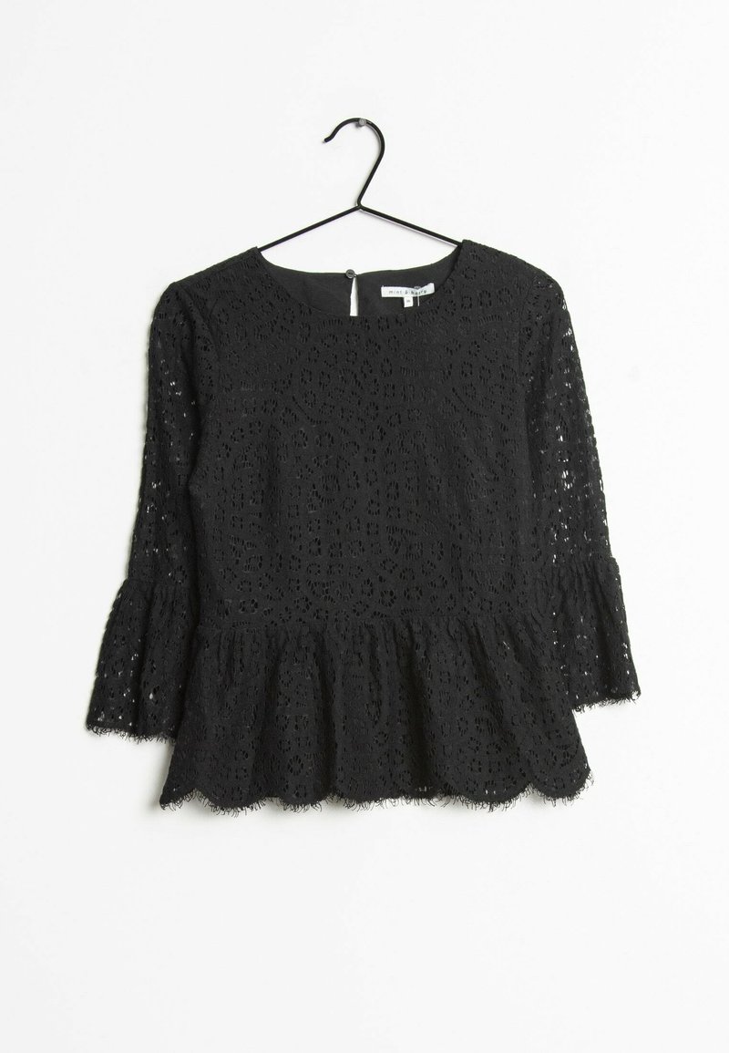 Top in pizzo nero con scollatura tonda, maniche a campana a tre quarti e orlo peplo. Presenta motivi floreali intricati e un bordo ondulato.