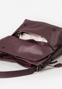 Borsa a spalla in pelle viola scuro con pattina fissata da due bottoni a pressione neri, con rivestimento interno in tessuto leggermente decorato.