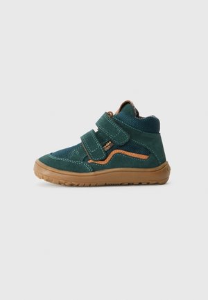 Dziecięcy ciemnozielony wysoki sneaker z brązową podeszwą, dwoma paskami na rzepy i pomarańczowym akcentem na prostym jasnym tle.