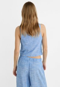 Modrý lněný crop top s uvolněným střihem, nastavitelnými ramínky a texturovaným povrchem, doplněný o odpovídající lněné kalhoty s elastickým pasem.