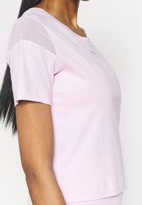 Rosa bomullströja med korta ärmar, med genomskinliga paneler på axlarna och en liten logodetalj nära halsringningen.