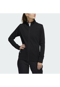 Schwarze Zip-Jacke mit langen Ärmeln, Stehkragen, strukturiertem Stoff, Seitentaschen und dezentem Logo am unteren Saum.