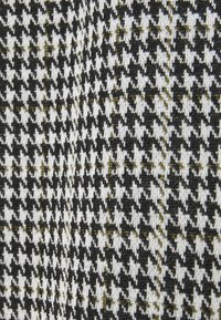 Houndstooth-tyg med ett mönster i svart, vitt och guld, med alternerande små och stora rutor. Texturerat stickat material.