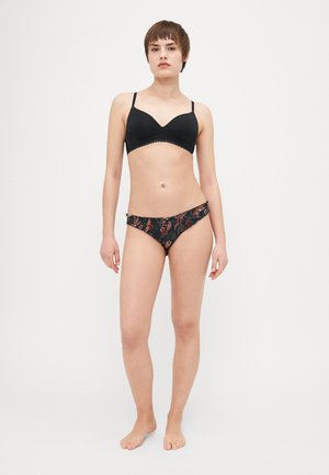 Sort polstret bh med bølget kant, parret med bikini-trusser med blomsterdesign. Materialet er blødt med en tætsiddende pasform. Neutral baggrund.