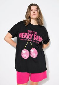 Černé oversized tričko s ohrnutými rukávy. Obsahuje výrazný růžový text "SAVE THE CHERRY DANCE" a grafiku dvou růžových diskotékových koulí.