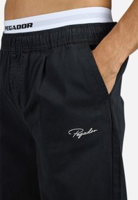 Black shorts made from lightweight fabric, featuring side pockets and a white elastic waistband with black lettering. Includes embroidered logo detail.