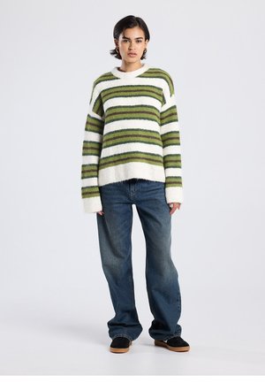 Striped sweater in soft knit with green and white horizontal lines; loose fit, ribbed cuffs and hem, paired with relaxed denim jeans.