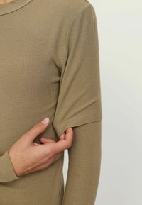 Lysbrun ribbet langærmet bluse med en afslappet pasform. Ærmet er let opklappet, hvilket viser en glat, blød tekstur.