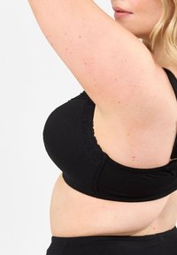 Svart tyg-bh med en slät textur, spetsdetaljer längs axelbanden och en sömlös design. Har justerbara band och en bred kant.