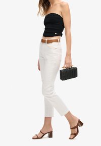 Woman walking wearing a black strapless top, white jeans with a brown belt, brown heeled sandals, and carrying a black woven handbag.