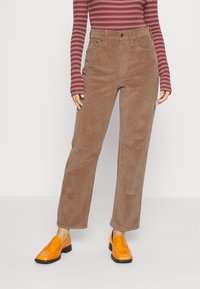 Bruna kordbyxorna med rak passform, hög midja, framfickor och kombinerade med ett par orangea slip-on skor. Randig långärmad tröja.