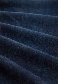 Mörkblå denim tyg med en slät textur, som har subtila variationer i nyans och vävda mönster, vikt i flera lager.