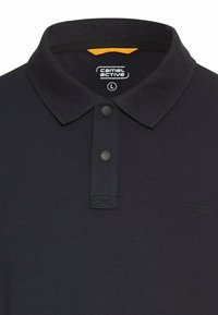 Polo Black Camel Active avec deux boutons noirs, un col côtelé et une étiquette taille L à l'intérieur de l'encolure.