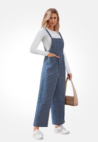 Blauw-witte gingham bretels met brede pijpen, voorzakken en verstelbare schouderbanden, gecombineerd met een effen langarmtop en sneakers.