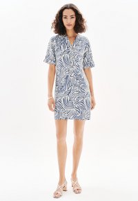 Vestido de manga corta en una tela ligera con un patrón abstracto de olas azules sobre un fondo blanco, con un detalle de botón en el escote.