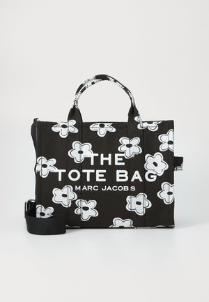 Svart Marc Jacobs toteväska med vita blommönster, dubbla handtag och en avtagbar axelrem, med texten "THE TOTE BAG".