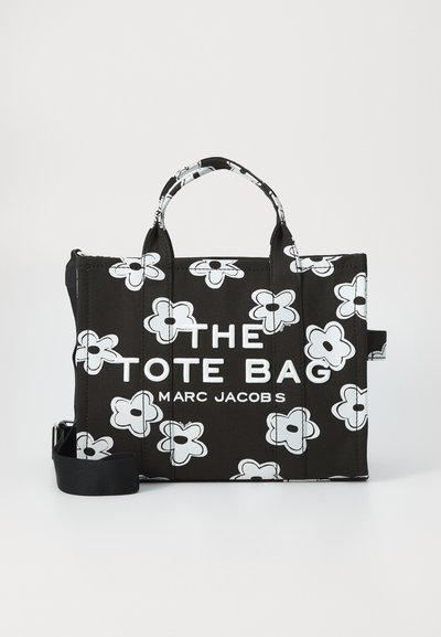 Svart Marc Jacobs toteveske med hvite blomstertrykkinger, doble håndtak og en avtakbar skulderrem, med teksten "THE TOTE BAG".