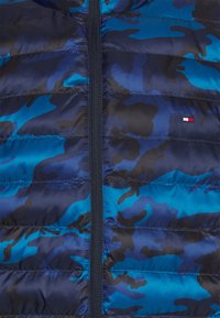 Gepolsterte Jacke in Dunkelblau mit Tarnmuster. Verfügt über einen Frontreißverschluss, ein strukturiertes Steppmuster und ein kleines Logo in Rot, Weiß und Blau.