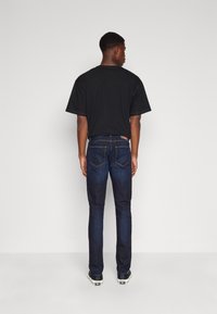 T-shirt noir à manches courtes associé à un jean en denim foncé. Le jean a une coupe classique et des coutures contrastées. Des baskets complètent le look.