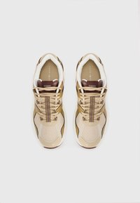 Baskets de sport beiges avec une tige en mesh et cuir, accents marron contrastants, lacets noués et logo sur la languette.
