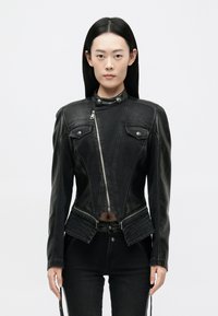 Must mustruudel nahkjakker, mis on sobiva disainiga, lukuga kinnitamine, kõrge krae ja kaks esikotti. Omab tekstuurilisi aktsente ja lühendatud hem.