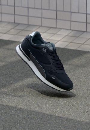 Zapatilla negra de cuero con detalles en gris, que presenta una suela blanca, punta redonda y diseño de cordones. Flotando sobre una superficie texturizada.