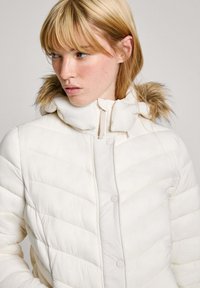 Witte pufferjack met een horizontaal chevrondesign, hoge kraag en afneembare bontafwerking op de capuchon. Zachte textuur en zichtbaar drukknoopsluiting.