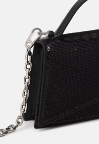 Sac à main noir avec surface texturée, poignée supérieure et bandoulière chaîne argentée attachée par un fermoir métallique sur fond blanc.